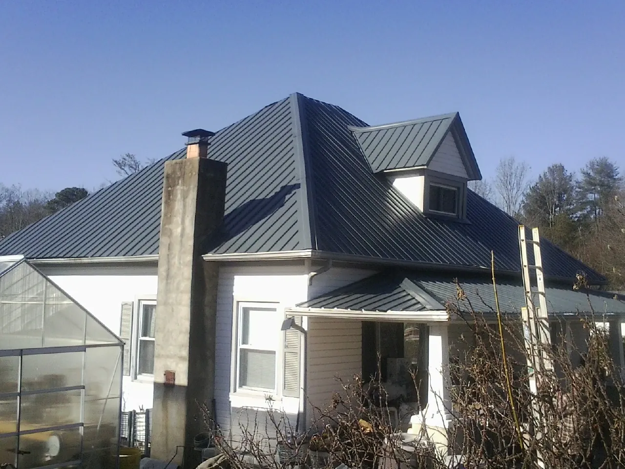 Dark blue standing seam metal roof on a white farmhouse with dormer — Slate & Tile Roof Repair by Roofing Brothers in Holcomb
