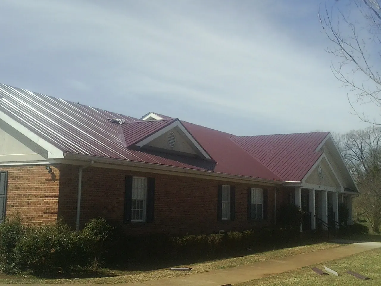 Red metal roof with gabled entries on a long brick building, from a Hail Damage Roof Repair job in Holcomb