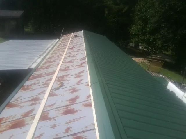Old rusted panels beside newly installed green metal roofing — Wind Damage Roof Repair by Roofing Brothers in Holcomb