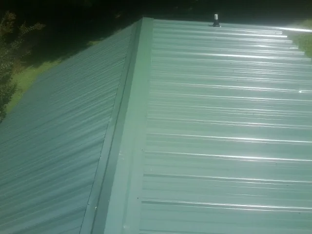 New green metal panels meeting at the ridge of a roof — Flat Roof Repair work by our crew in Holcomb