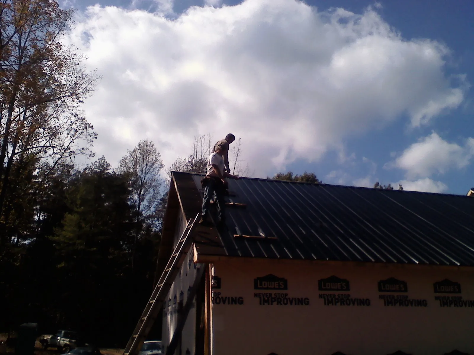Roofer fastening dark metal panels high against a cloudy sky, from a Roof Inspection job in Holcomb