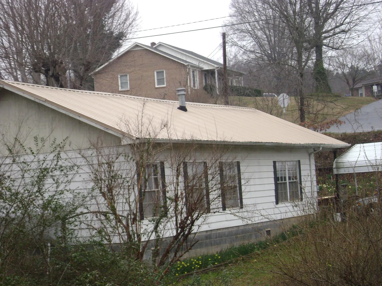 Tan metal roof on a white sided house set into a hillside — Commercial Roofing by Roofing Brothers in Holcomb