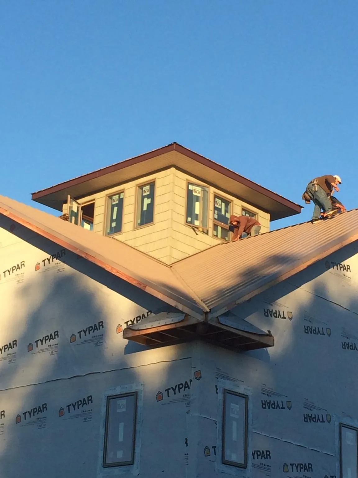 Roofers working around a rooftop cupola on a new metal roof at sunset — Roof Waterproofing in Holcomb by Roofing Brothers